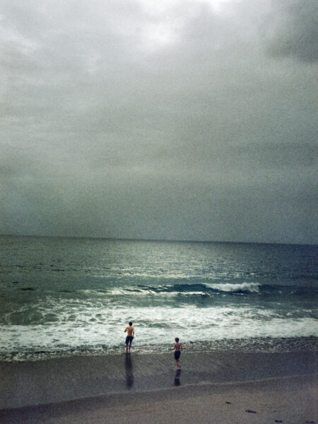 Fine art picture showing two boys running into the water on a beach in misty and dark weather