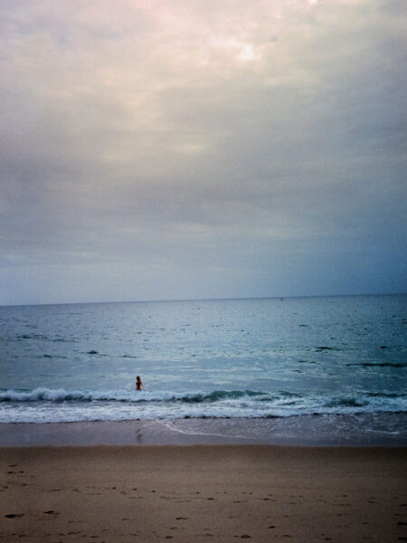 Fine art picture showing a beach with a young woman taking a bath in a calm sea in the evening